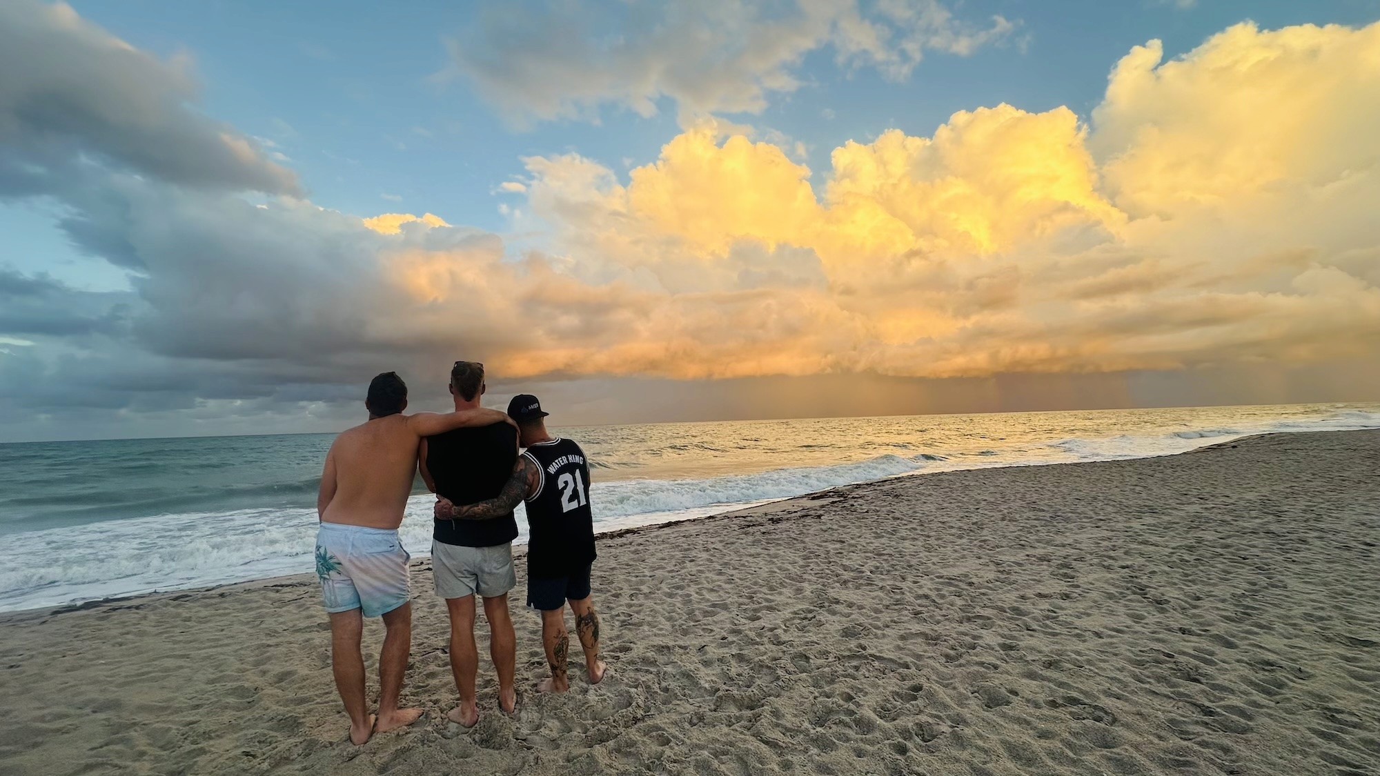 Three men standing together on the beach at sunrise